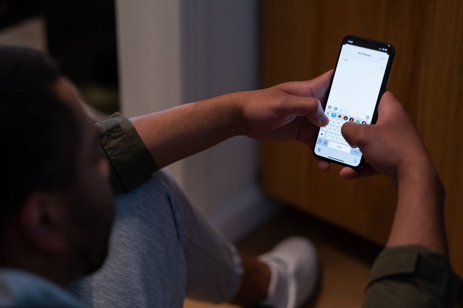 Uomo seduto che scrive un nuovo messaggio di testo sullo schermo dello smartphone tenuto con entrambe le mani