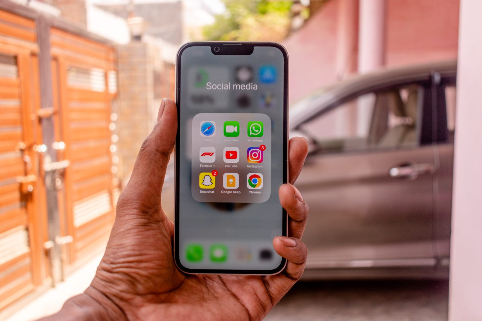 Main tenant un iPhone affichant un dossier d'applications de messagerie et de réseaux sociaux