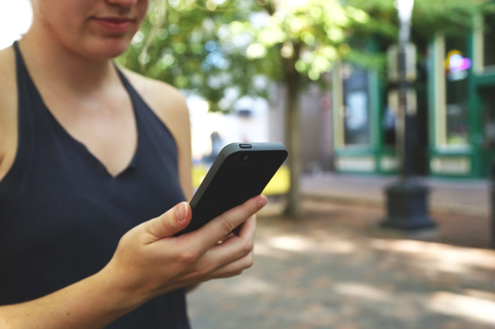 Jeune femme tenant un smartphone noir dans la rue, écran tourné vers elle