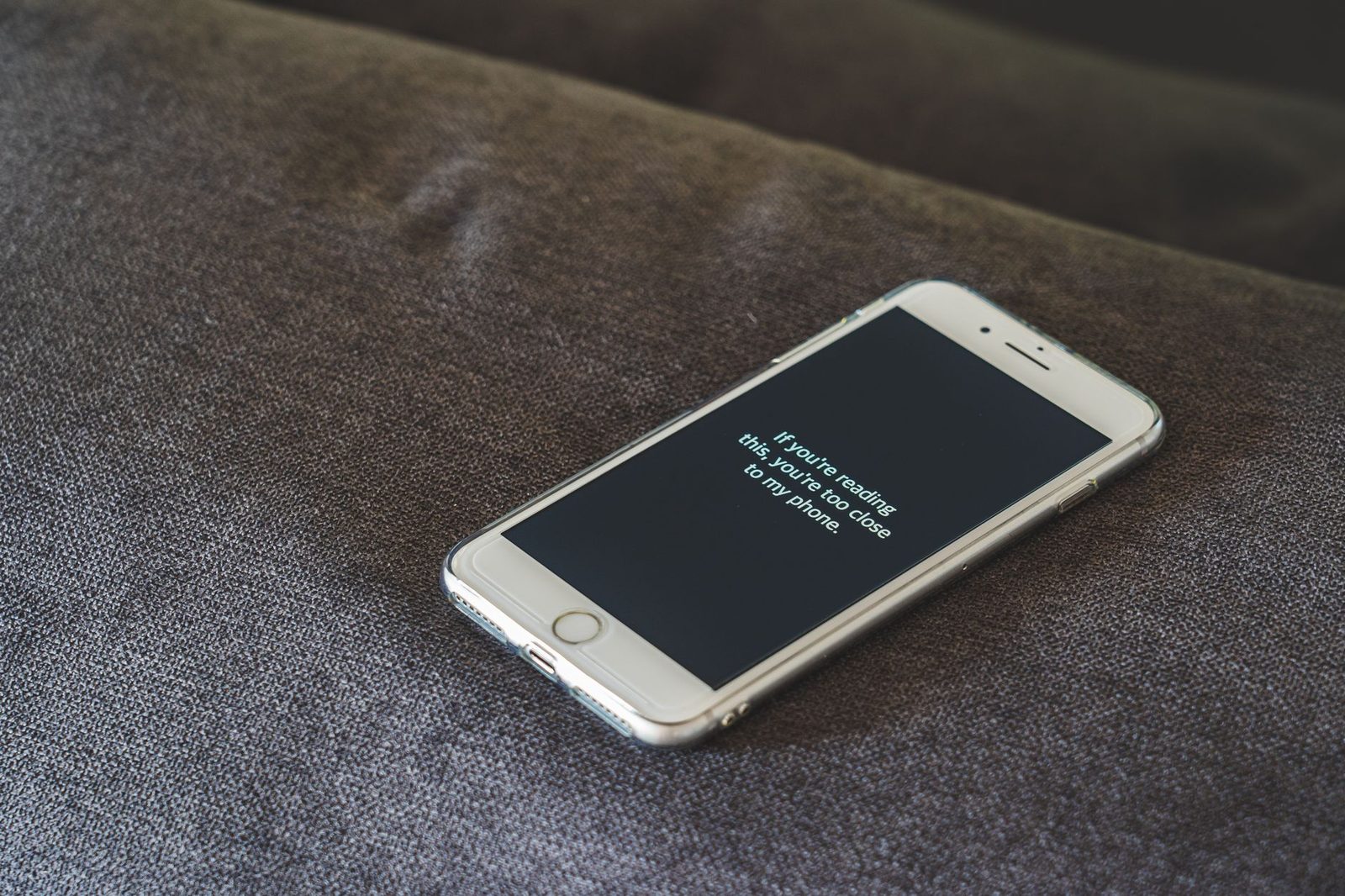 Weißes iPhone auf einem grauen Stoffsofa, das auf schwarzem Bildschirm eine Textnachricht anzeigt