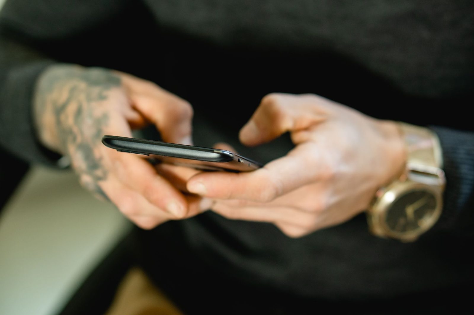 Primo piano delle mani di un uomo tatuato che digita un messaggio su uno smartphone nero