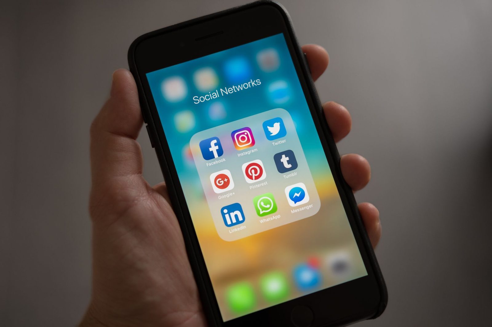 Mano che tiene un iPhone con visualizzata una cartella «Social Networks» contenente app di messaggistica