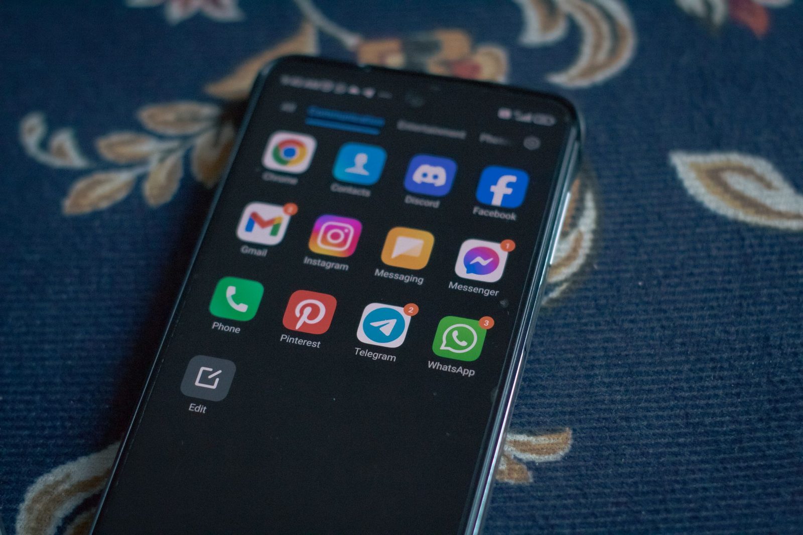 Smartfon leżący na niebieskiej tkaninie, wyświetlający ikony aplikacji do wiadomości i SMS-ów z powiadomieniami