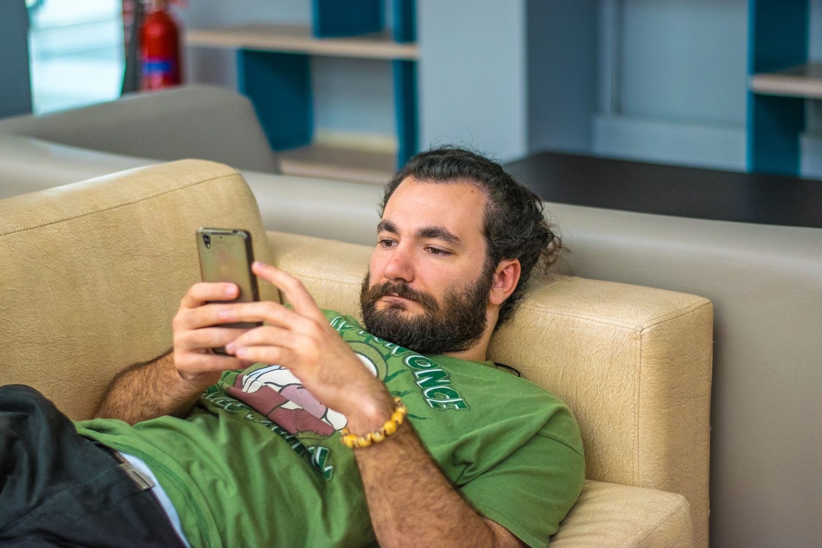 Bearded man lying on a sofa, reading a message on his mobile phone
