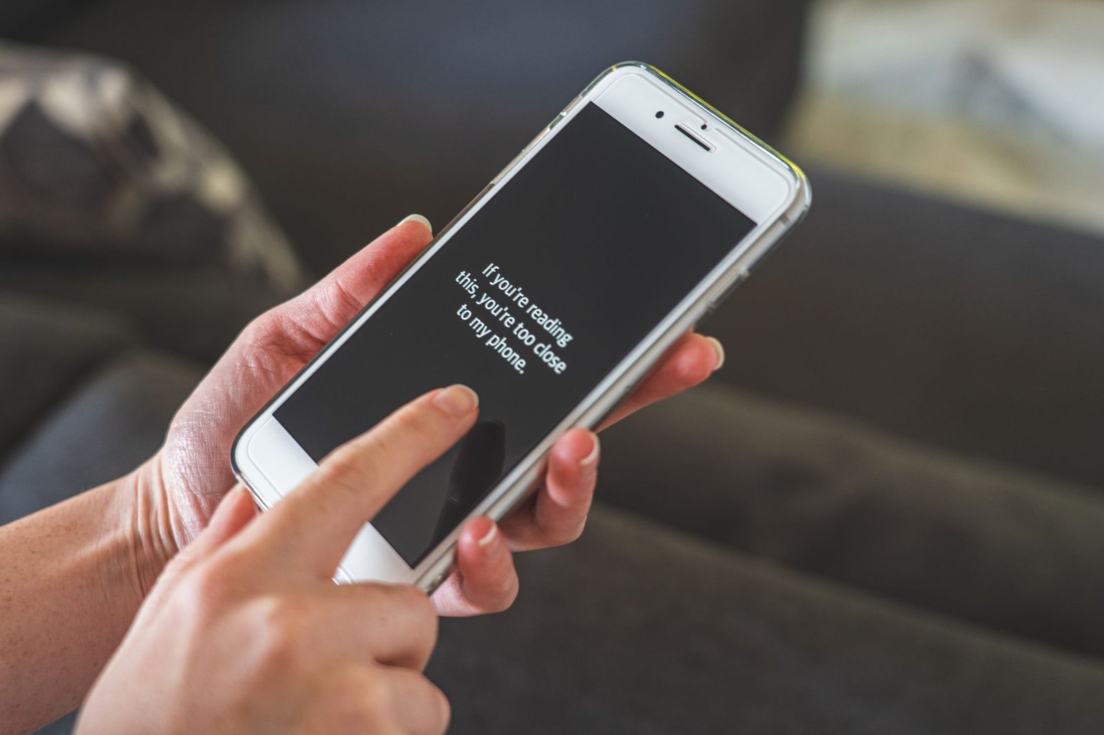 A woman's hands holding a white smartphone displaying a text message on screen, sitting on a sofa