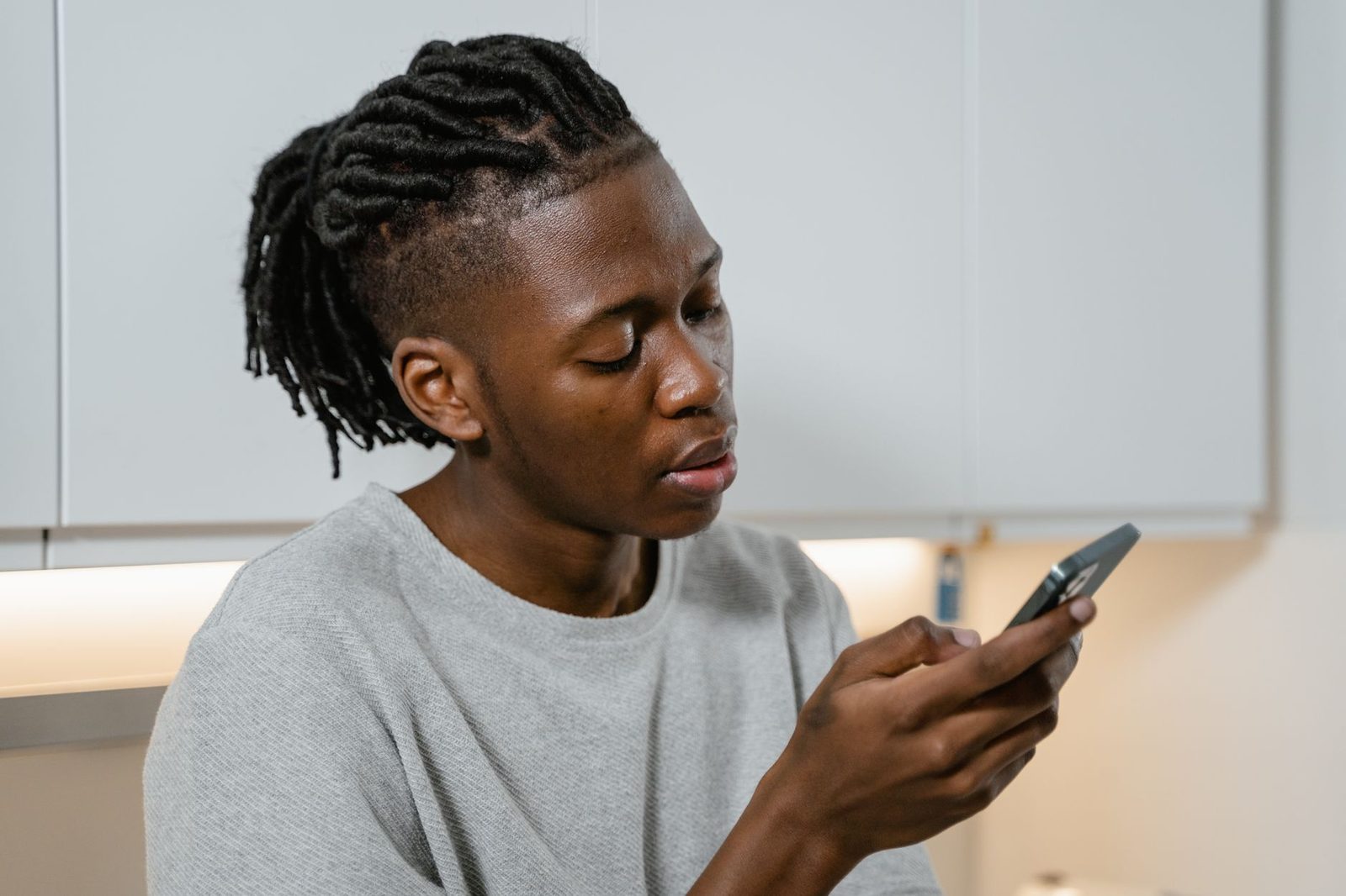 Man in a grey sweater reading a message attentively on his mobile phone in a kitchen