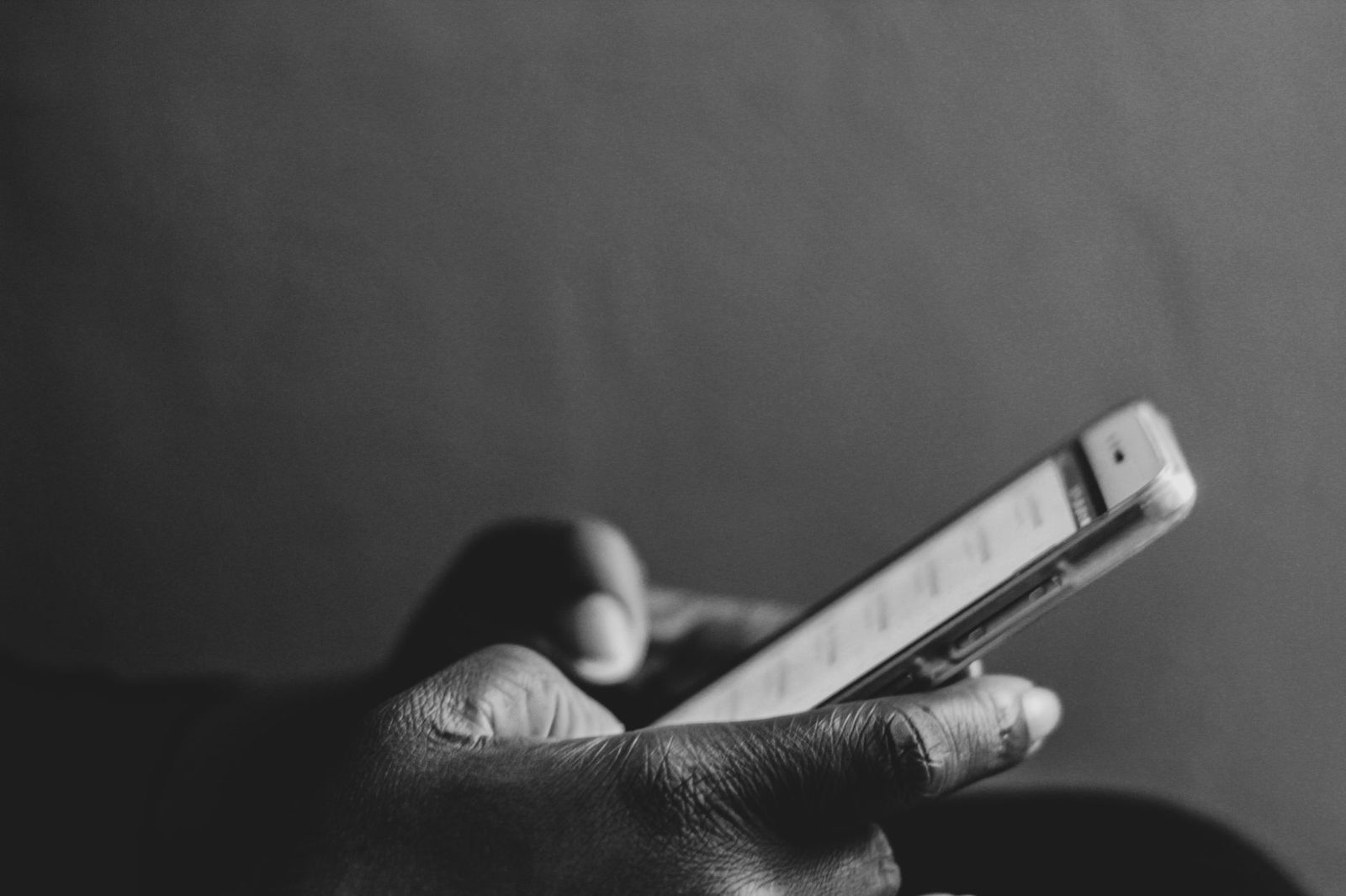 Foto in bianco e nero di una mano che tiene uno smartphone acceso davanti a uno sfondo scuro