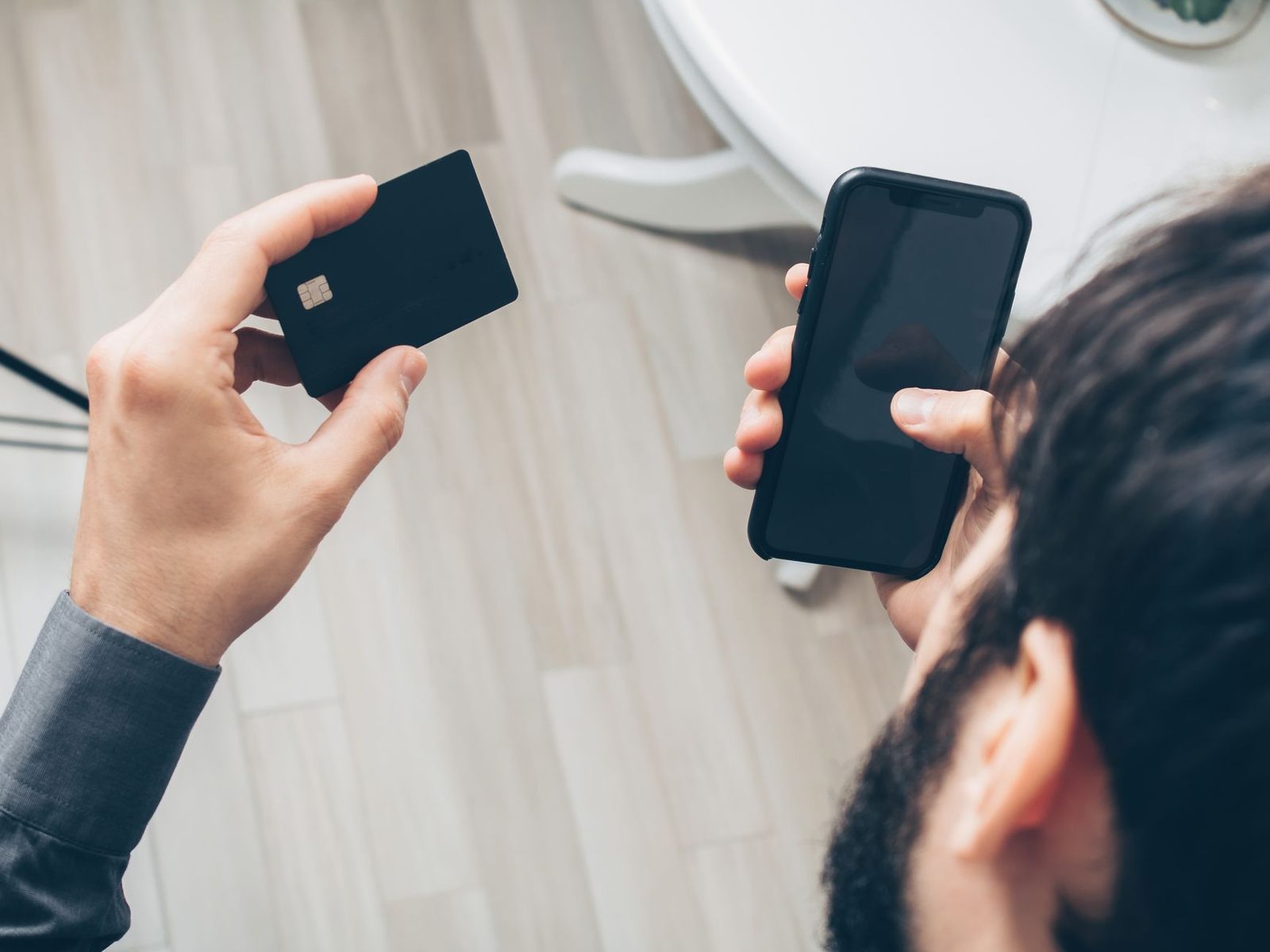 Hombre sosteniendo una tarjeta bancaria negra en una mano y un smartphone con la pantalla apagada en la otra