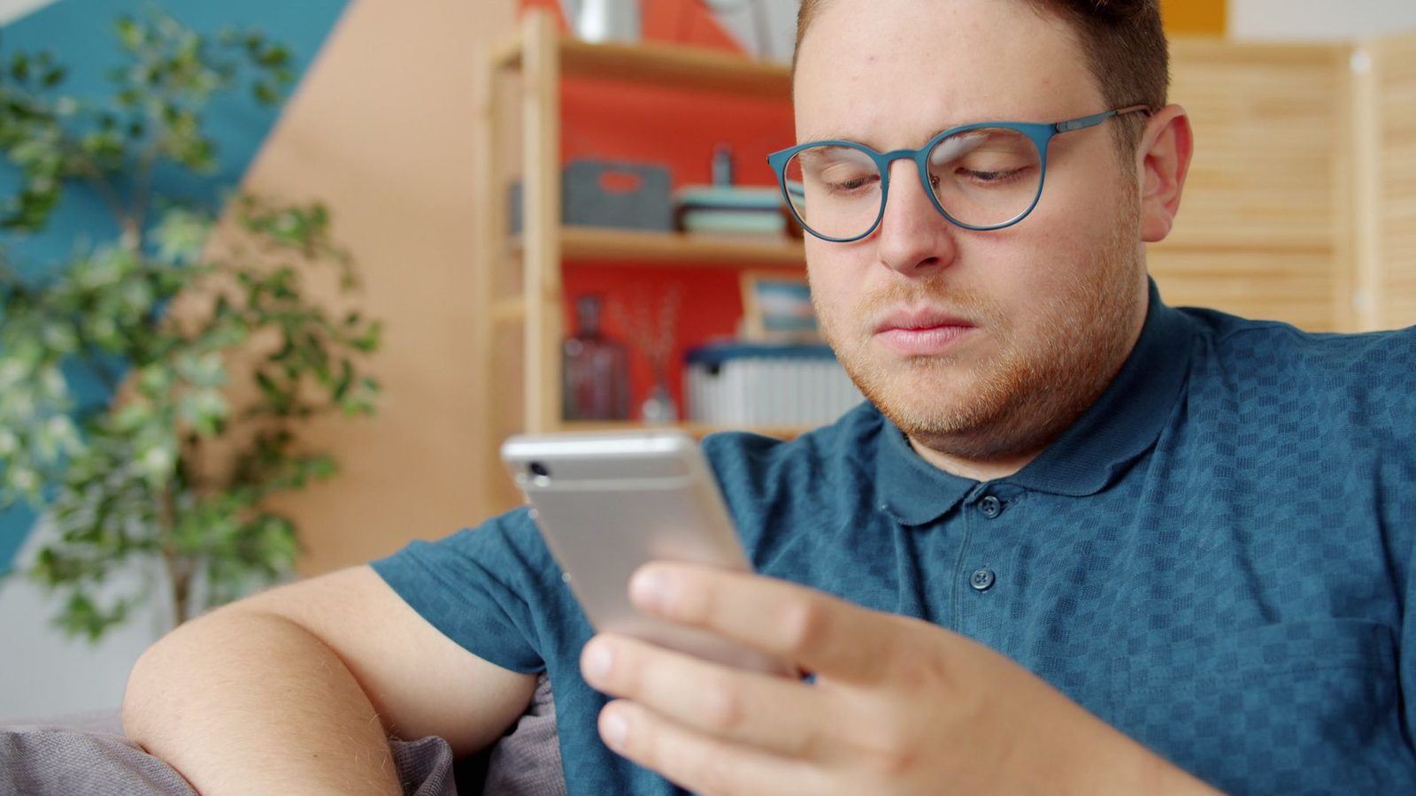 Homme à lunettes assis dans un salon, l'air perplexe, lisant un message sur son smartphone