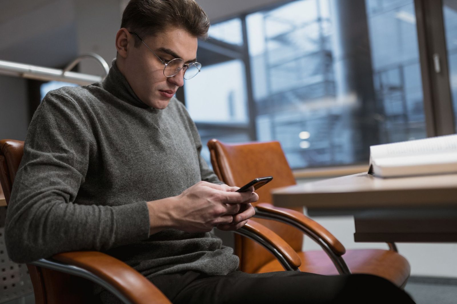 Homme à lunettes assis dans un fauteuil, consultant un message sur son smartphone dans un bureau