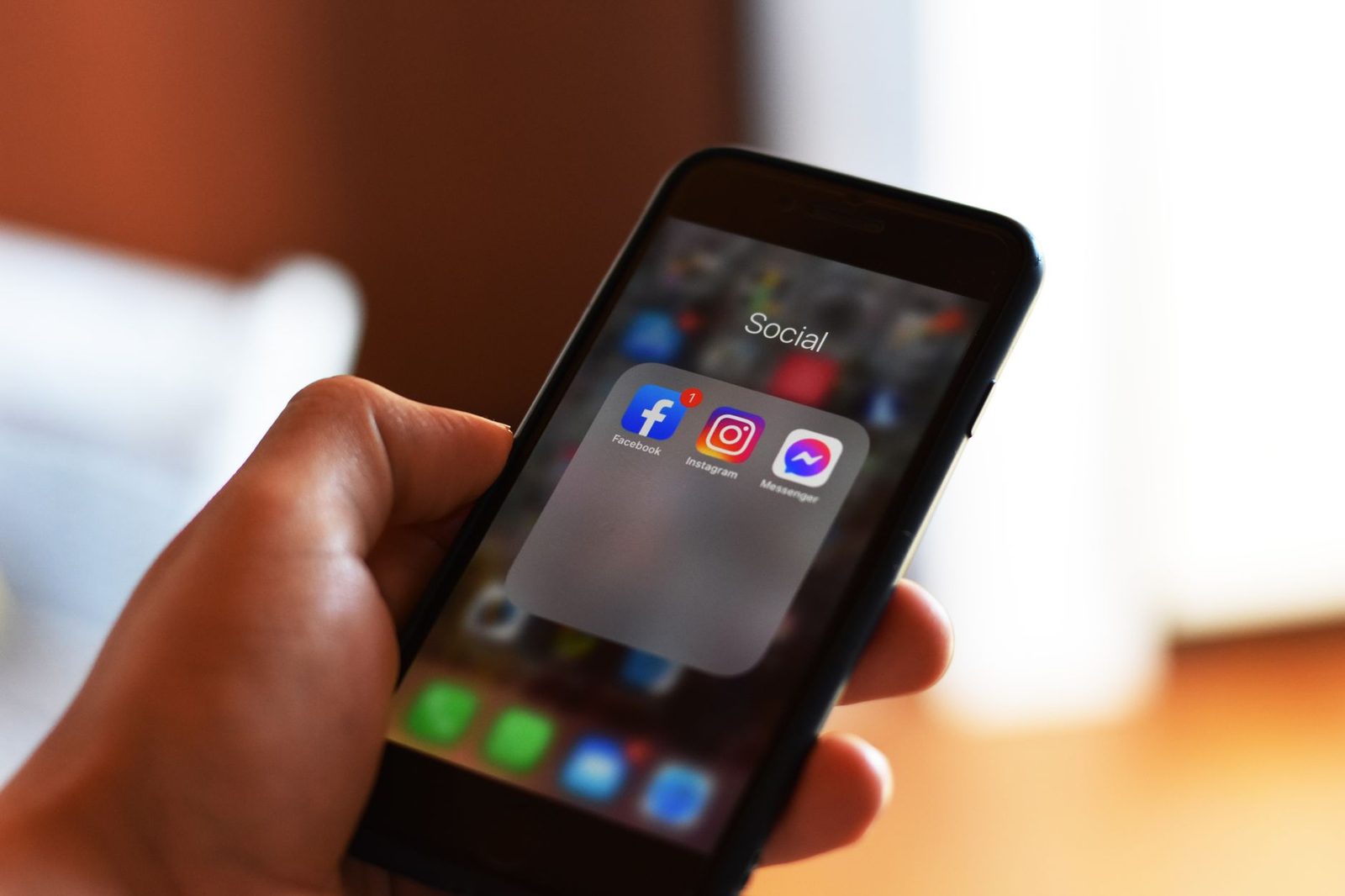 Mano che tiene uno smartphone con una cartella di app di social network visualizzata sulla schermata iniziale