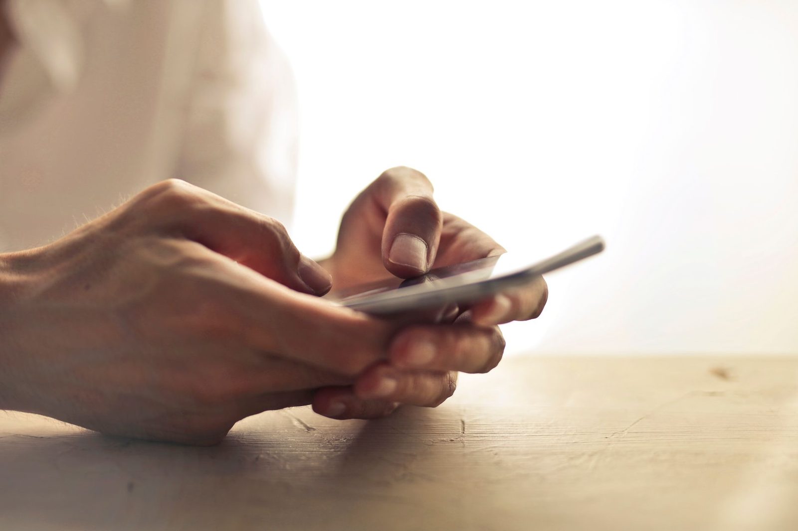 Primo piano sulle mani di una persona che consulta uno smartphone appoggiato su un tavolo di legno