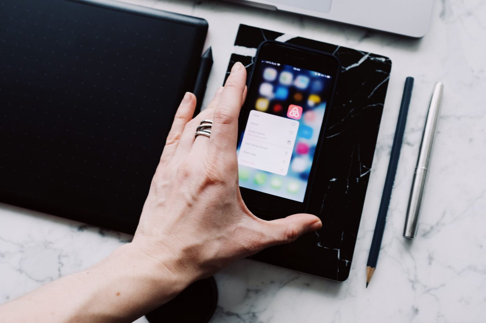Mano che tiene uno smartphone appoggiato su una scrivania in marmo, schermata iniziale con un menu di applicazioni