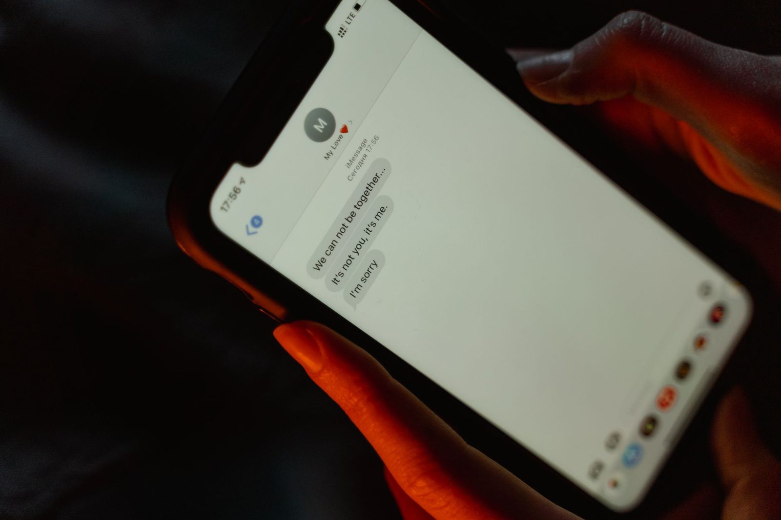 Dłonie trzymające smartfon z wyświetloną rozmową SMS, w półmroku