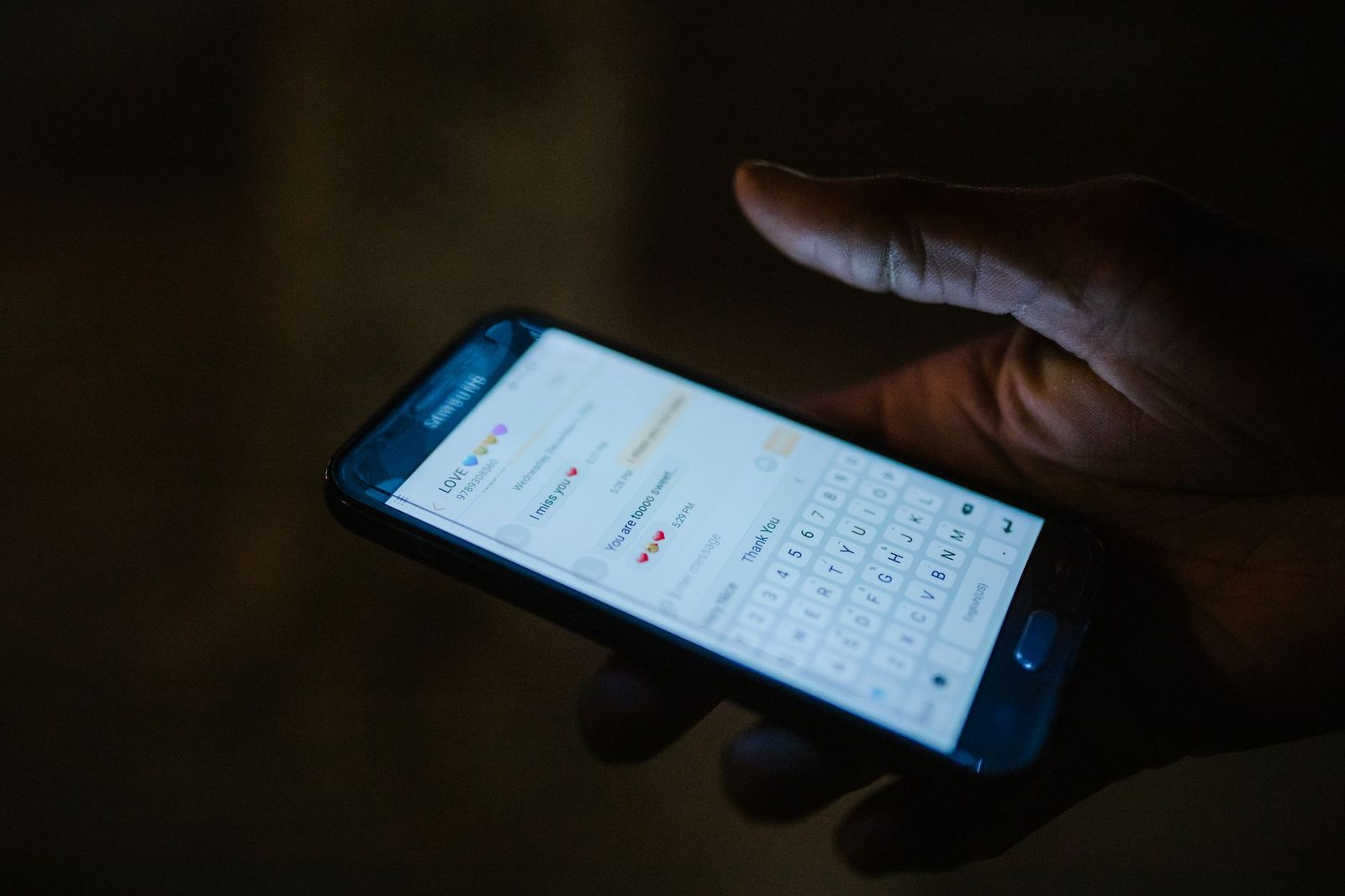 Dłoń trzymająca w ciemności włączony smartfon z widoczną rozmową SMS i klawiaturą