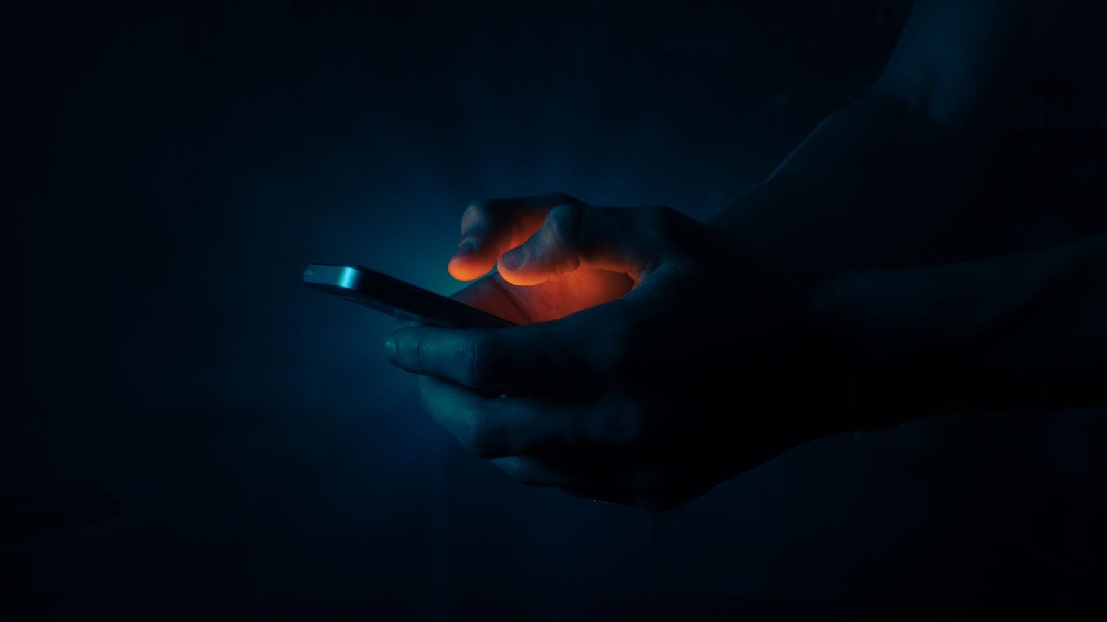 Mains tenant un smartphone dont l'écran éclaire les doigts dans l'obscurité