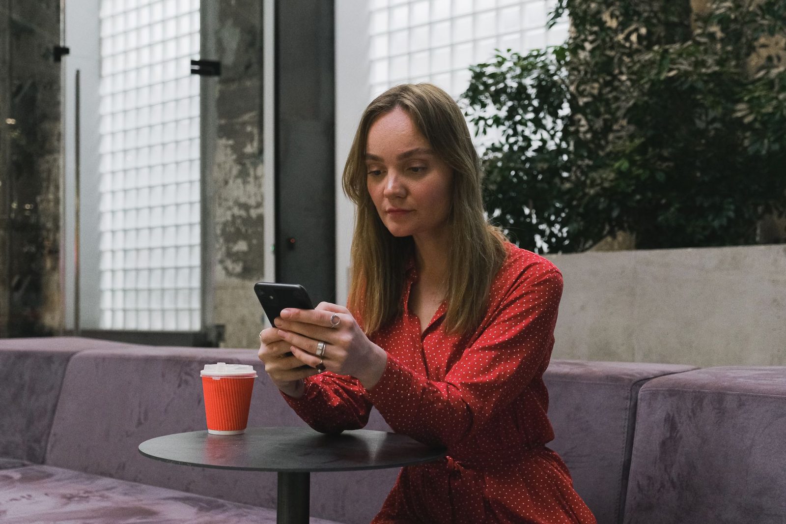 Jeune femme en robe rouge consultant son smartphone, assise à une table avec un gobelet de café