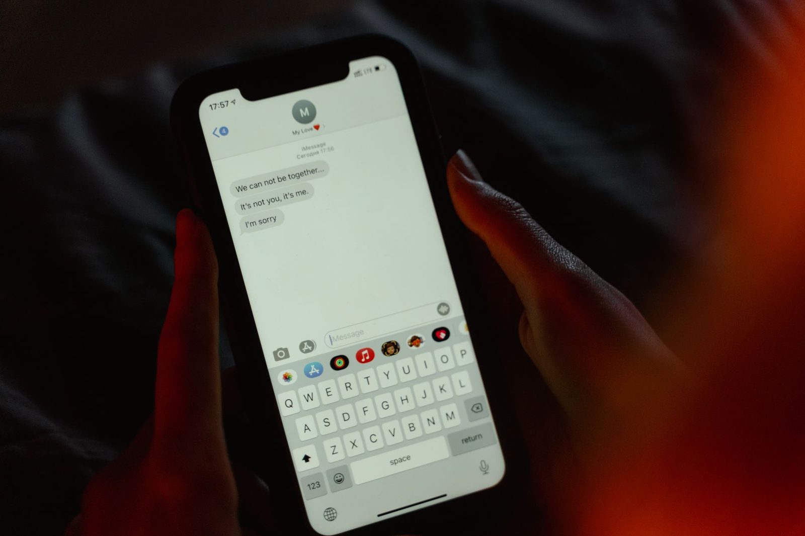 Mani che tengono uno smartphone con una conversazione di SMS sullo schermo, nella penombra