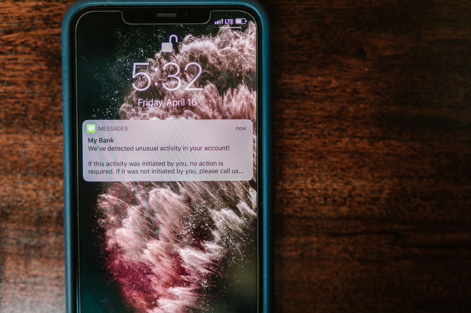 Smartphone sobre una mesa de madera mostrando en la pantalla bloqueada una notificación de SMS con una alerta bancaria