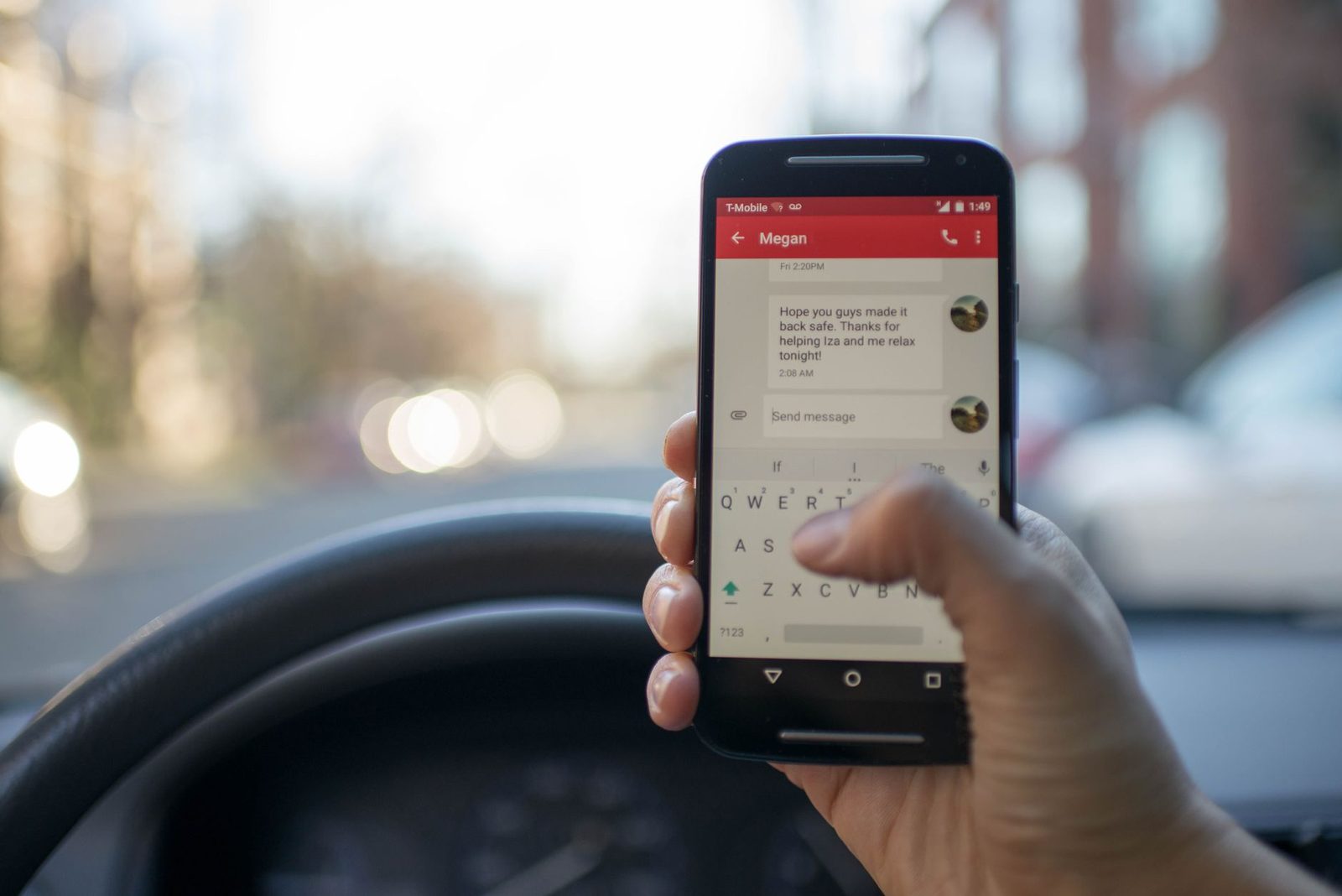 Mano sosteniendo un smartphone que muestra una conversación de SMS, al volante de un coche