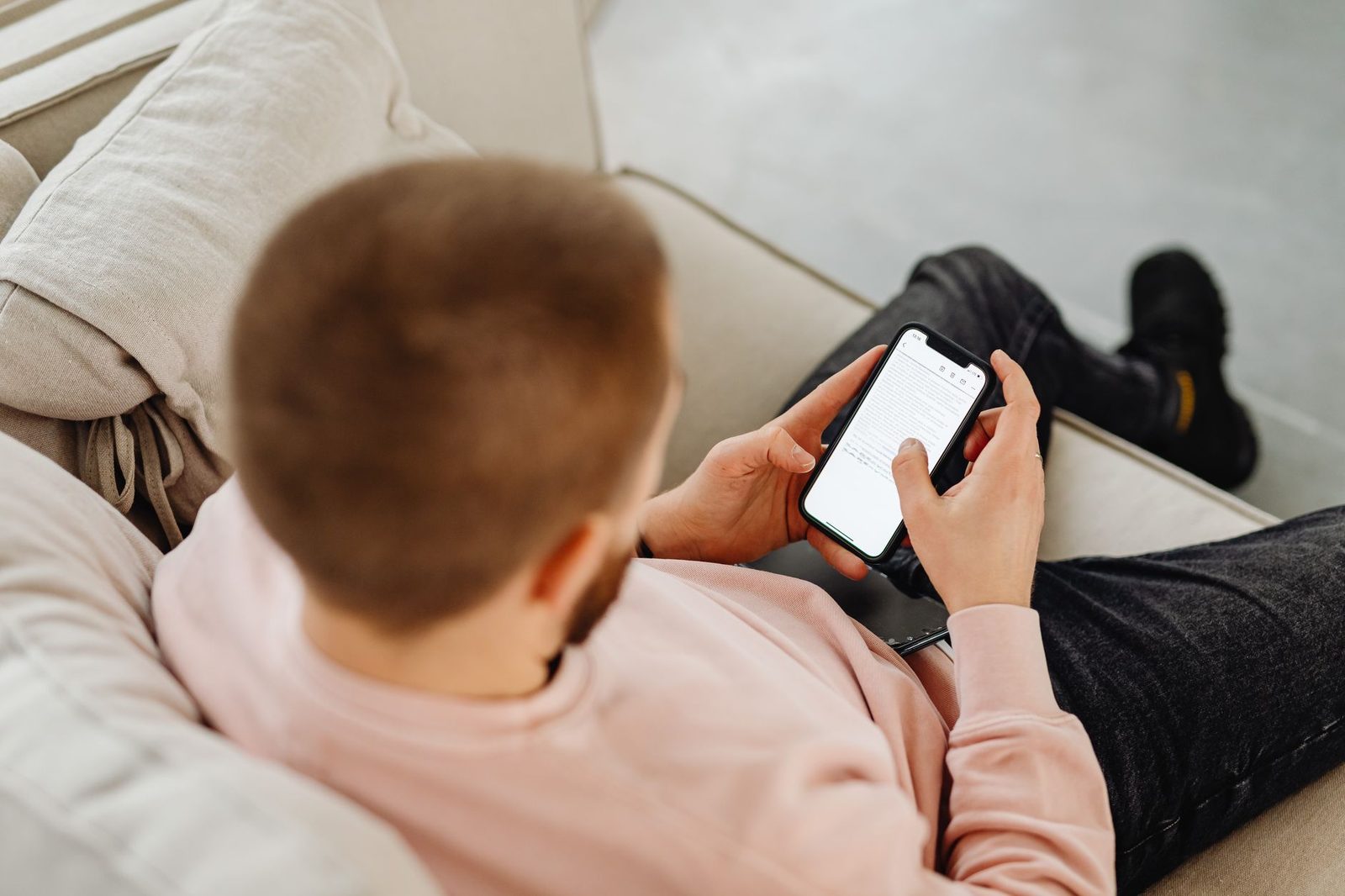 Man sitting on a sofa reading a message on his smartphone screen, seen from behind