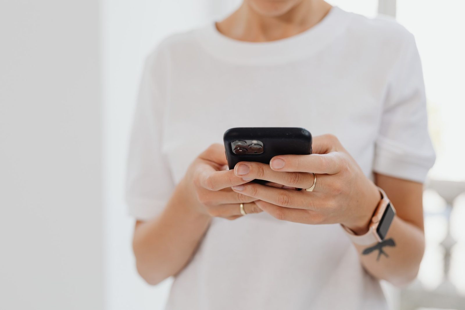 Mujer con camiseta blanca sosteniendo un smartphone negro entre las manos y mirando la pantalla