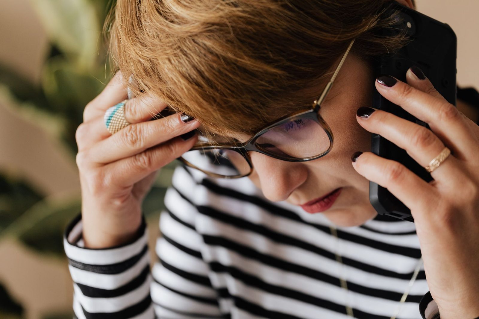 Femme à lunettes et pull rayé, l'air préoccupé, tenant un smartphone contre son oreille