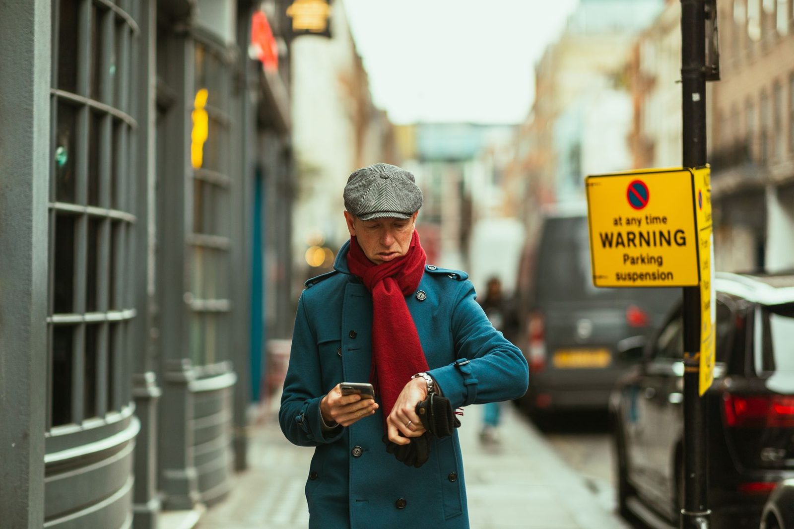 Homme en manteau bleu et écharpe rouge consultant son téléphone portable dans une rue