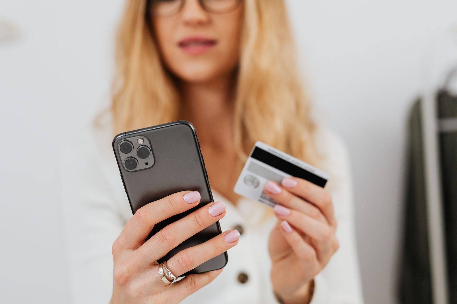 Femme tenant un smartphone dans une main et une carte bancaire dans l'autre, visage flou en arrière-plan
