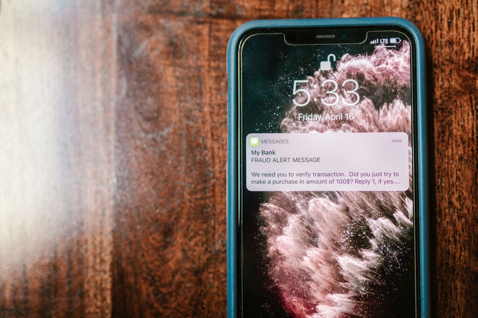 Smartphone posé sur une table en bois affichant un SMS frauduleux d'alerte bancaire sur l'écran verrouillé