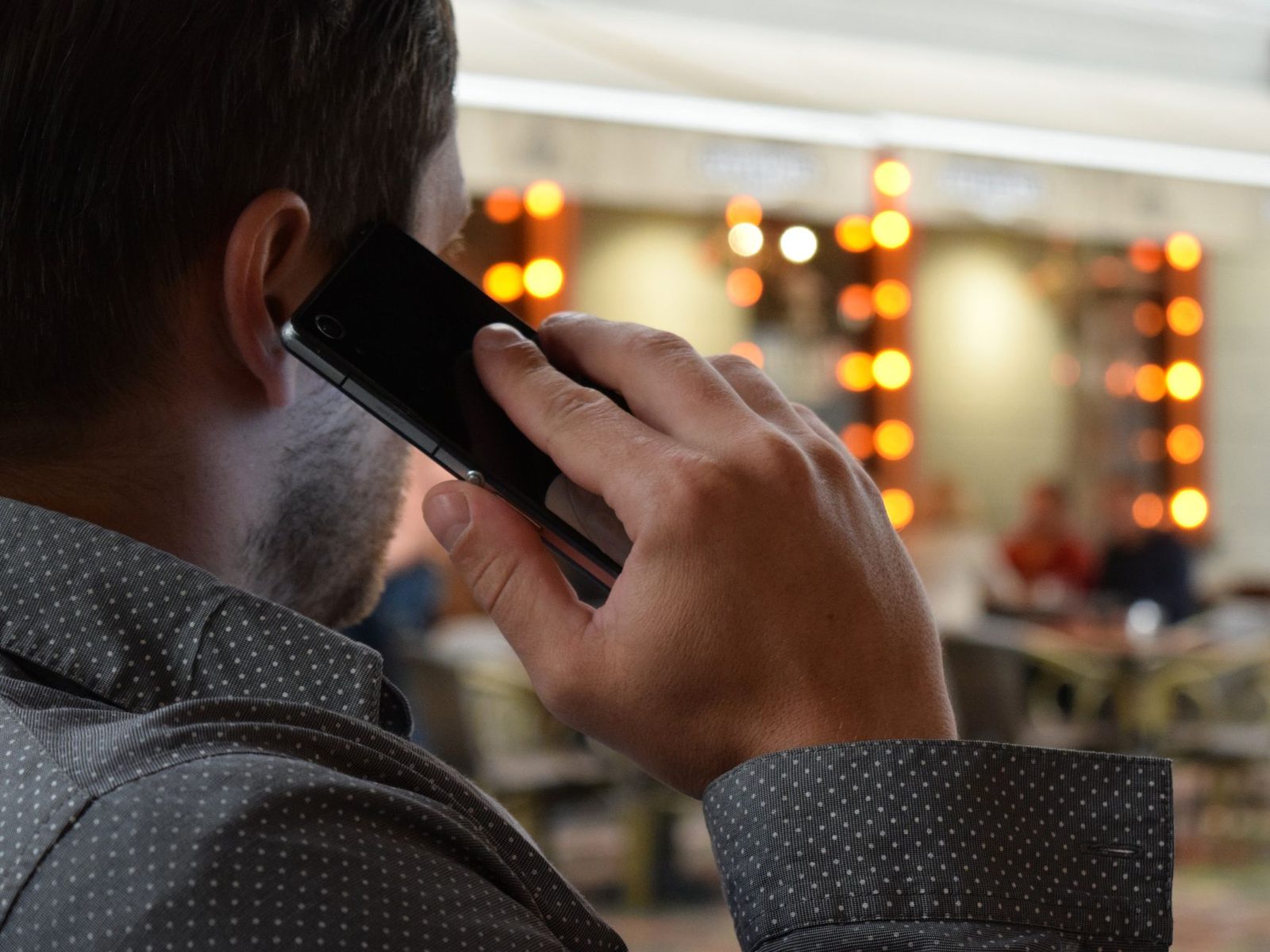 Homme de dos passant un appel avec un smartphone noir tenu contre son oreille, dans un lieu éclairé