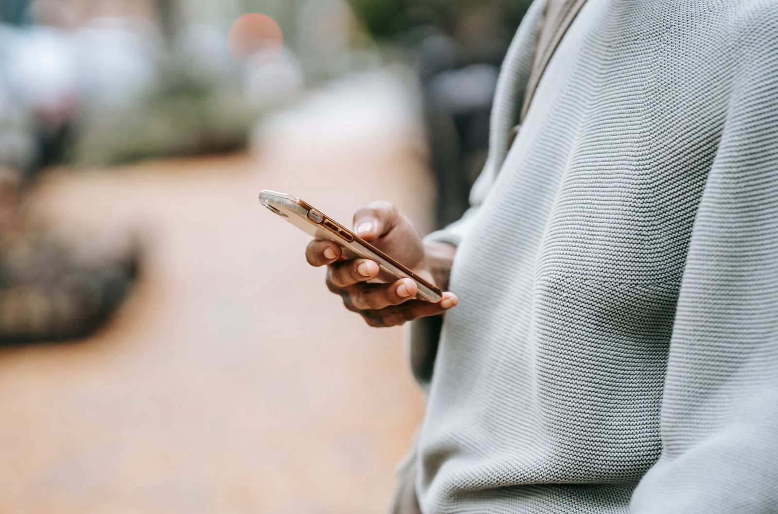 Gros plan sur les mains d'une personne tenant un smartphone dans la rue, pull gris en maille