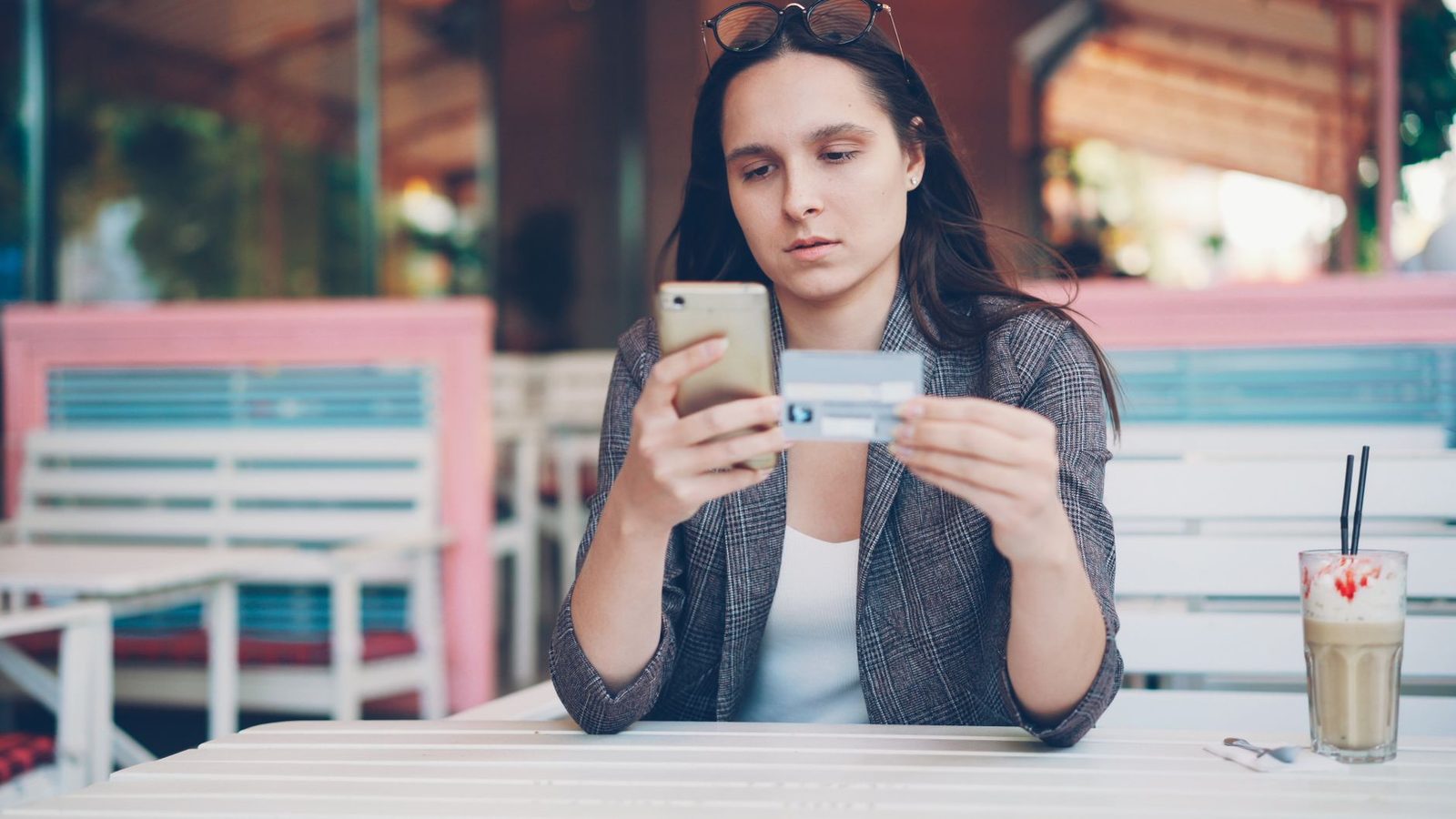 Jeune femme assise à une terrasse de café tenant un smartphone et une carte bancaire