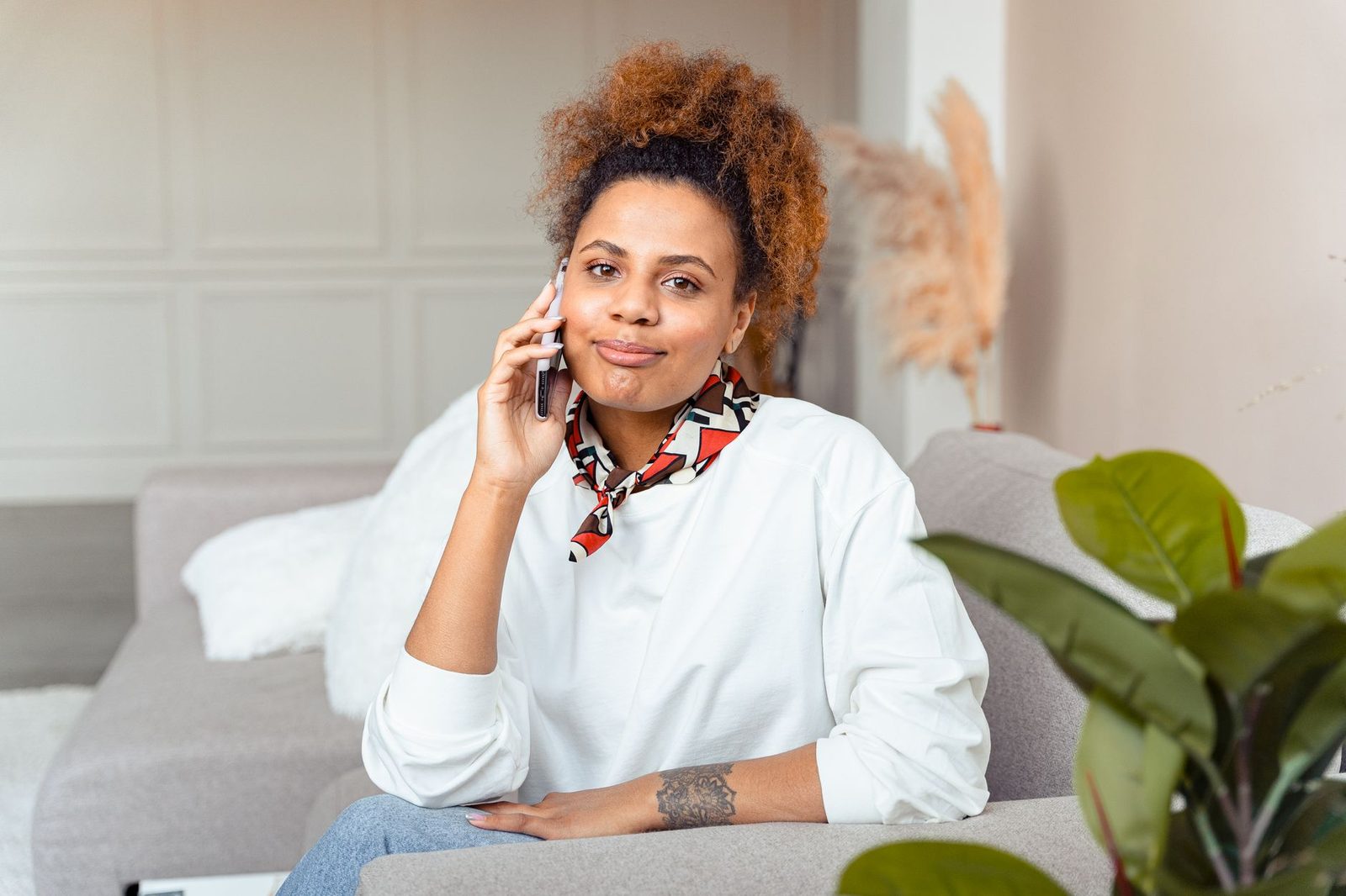Woman sitting on a sofa in a living room, talking on her smartphone held to her ear