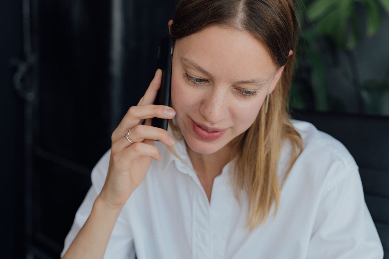 Young woman in a white shirt taking a call on a black smartphone held to her ear