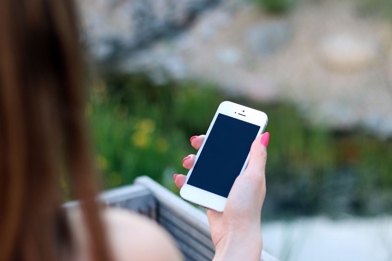 Woman holding a white smartphone with the screen switched off, seen over the shoulder, outdoors