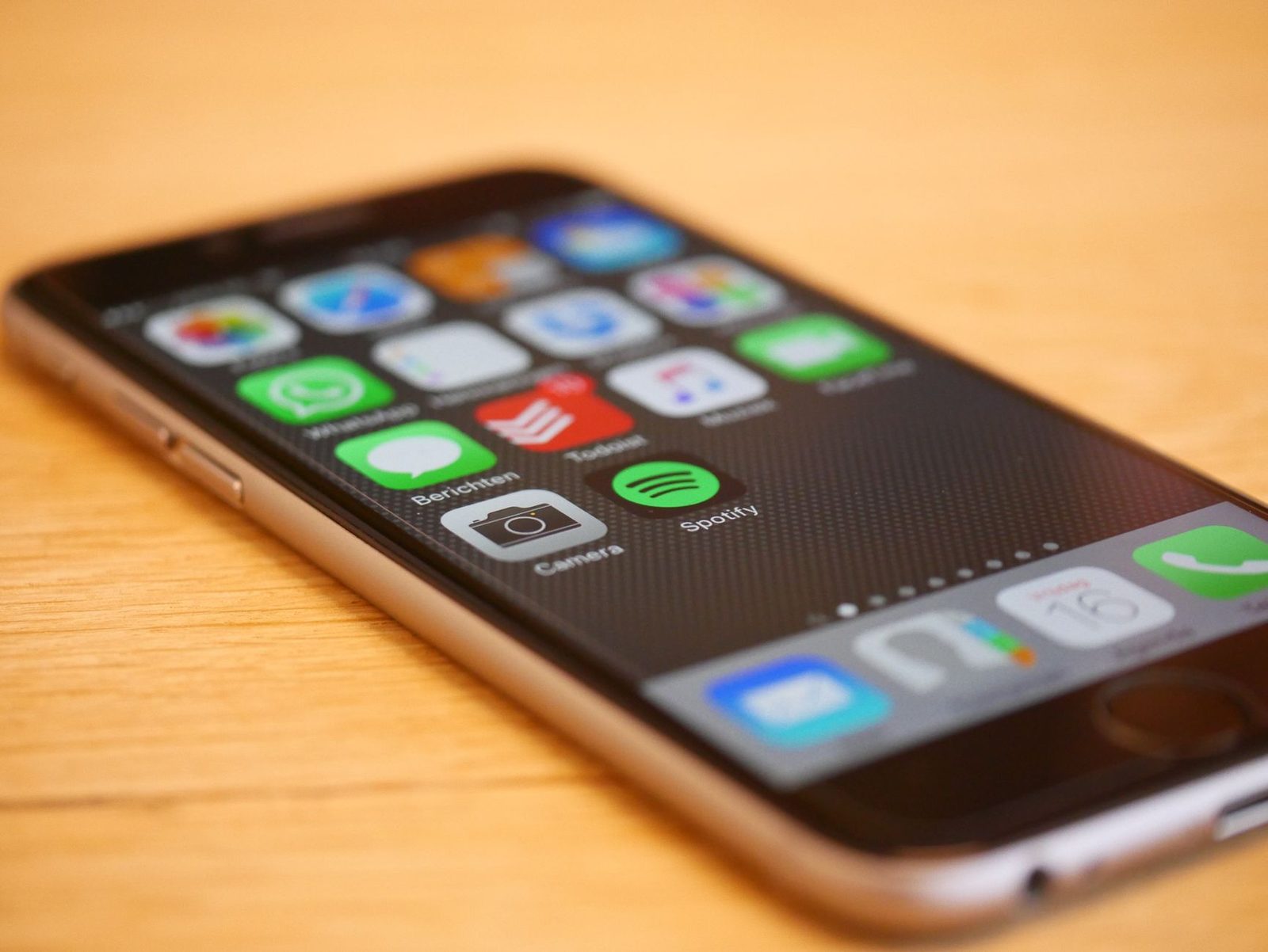 Smartphone lying on a wooden table, home screen showing app icons including the messaging app